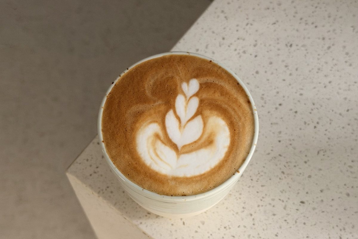 A flat white with rosetta latte art resting on a pale stone counter.