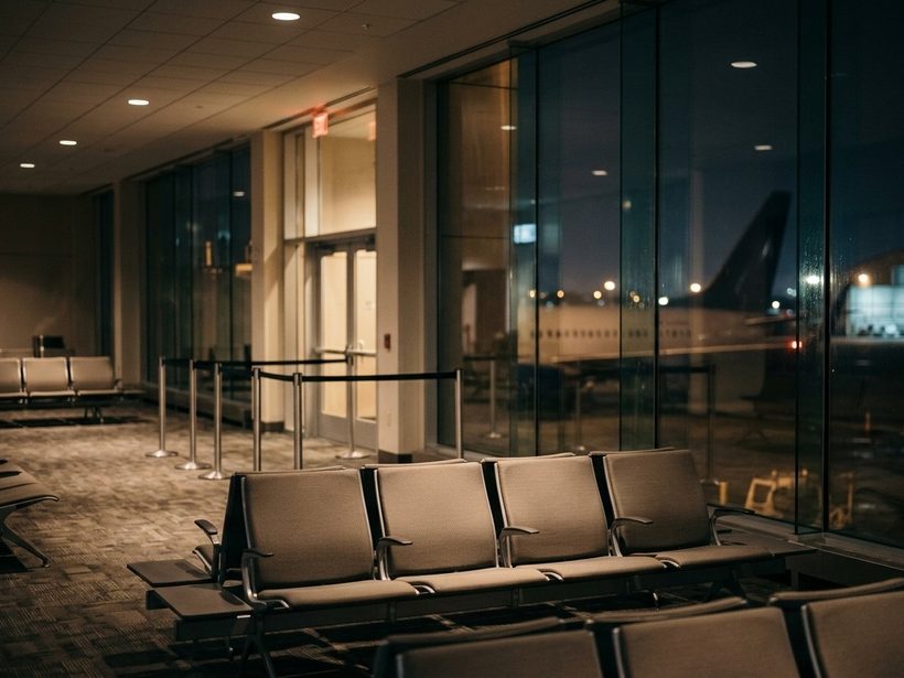 Empty airport gate seats by a terminal window at night, an aircraft waiting beyond the glass.